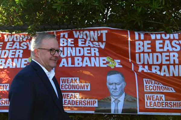 Anthony Albanese walks past election posters criticising him