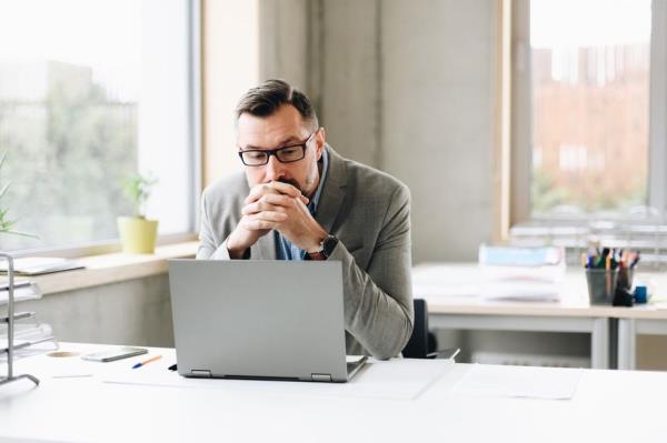 Thoughtful middle aged handsome businessman in shirt working on laptop computer in office