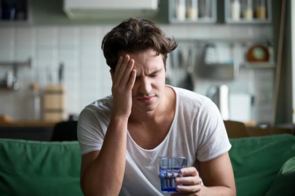 Young man suffering from strong headache sitting with glass of water, touching his head.