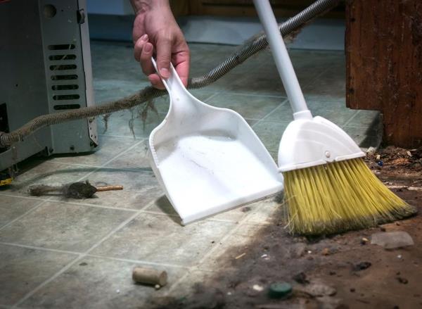 A man sweeps dust up from underneath a fridge