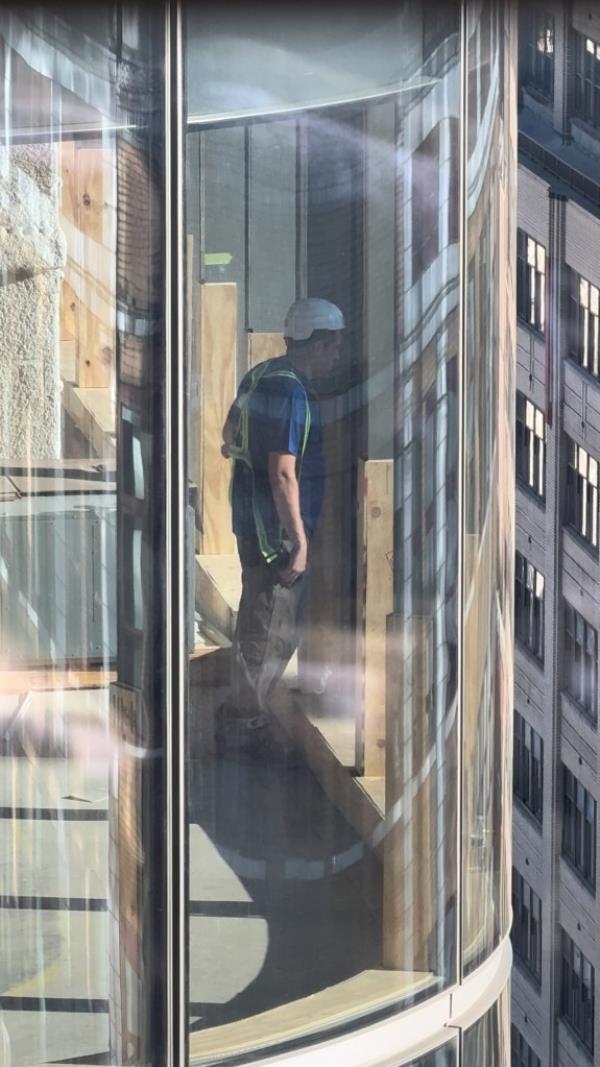 Co<em></em>nstruction worker in a hard hat peering from Two Manhattan West skyscraper towards Fashion Institute of Technology's dorms.