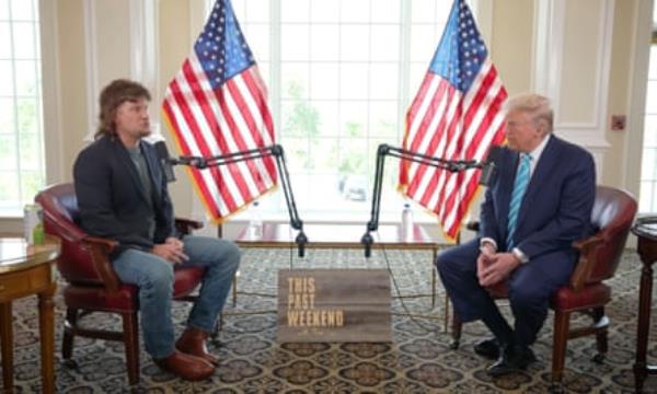 two men sit across from each other with american flags between them