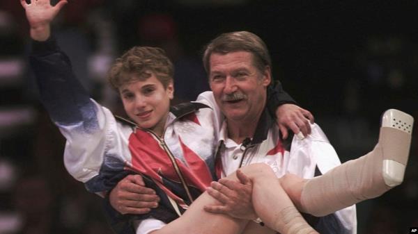 FILE - USA's Kerri Strug is carried by her coach, Bela Karolyi, as she waves to the crowd on her way to receiving her gold medal for the women's team gymnastics competition, at the Summer Olympic Games in Atlanta, July 23, 1996.