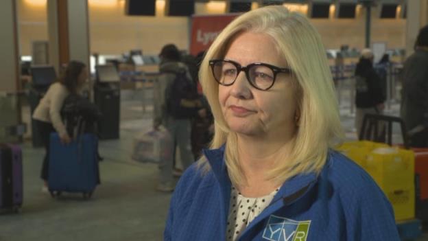 Vancouver Internatio<em></em>nal Airport's president and CEO, Tamara Vrooman, wears thick black glasses and stands in the terminal wearing a blue zip-up sweater with YVR's logo.