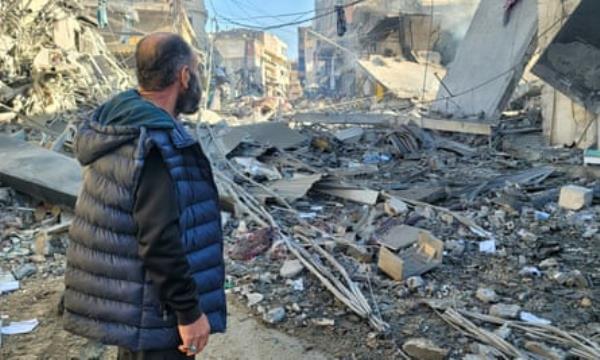 A man stands looking towards rubble and debris on a street